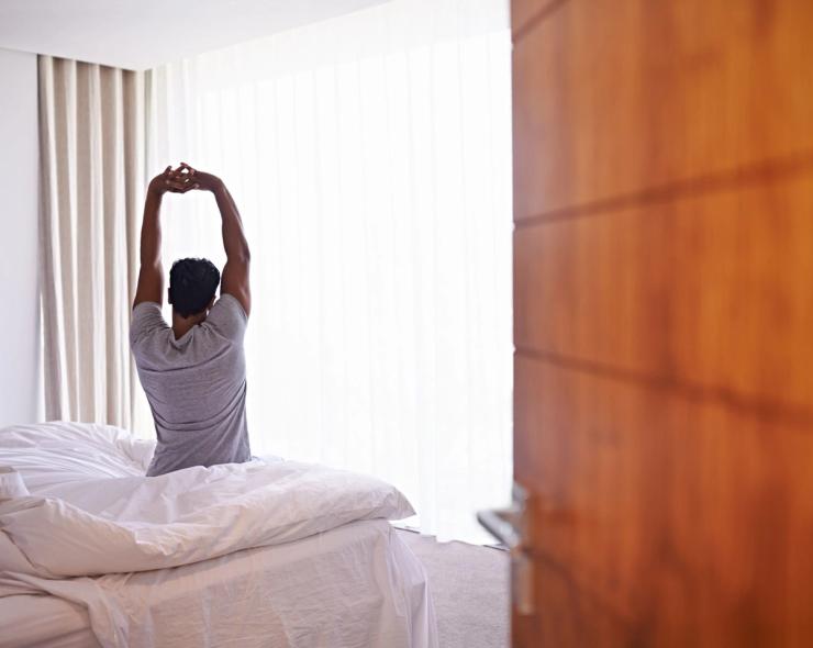 A person stretches while sitting on a hotel bed. 