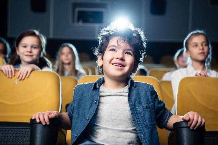 A boy with dark hair and dark eyes watching a movie in a theater.