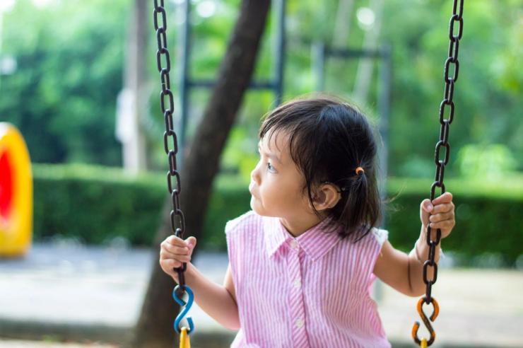 Young girl on a playground swing. She is wearing a hearing aid