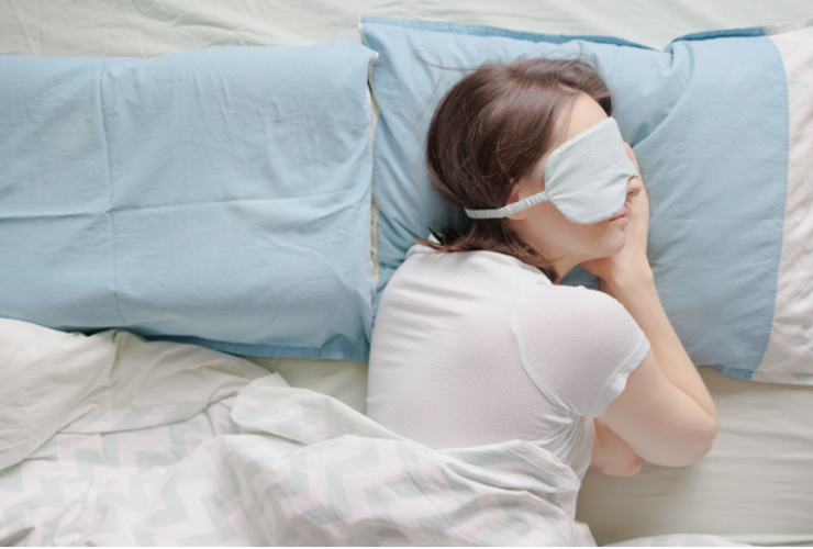 Young woman in bed wearing sleep mask to cope with jet lag.