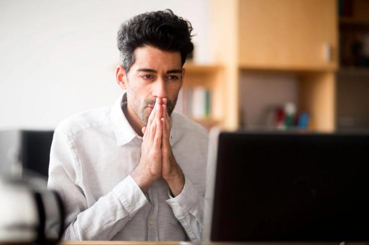 A white man with dark hair is looking hopefully at a computer. 