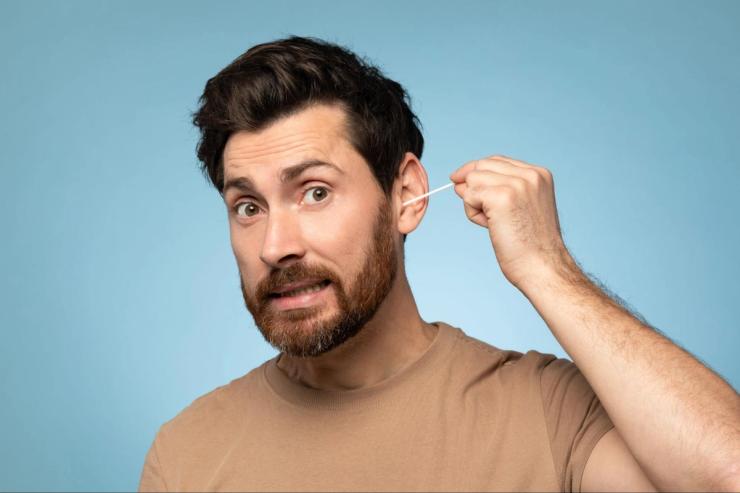 Man using a cotton swab in his ear showing unsafe ear cleaning habits that may increase risk of hearing damage