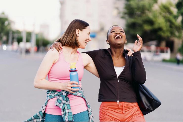 Two women laughing and walking together outdoors after exercise, supporting overall wellness and healthy lifestyle habits that can help protect hearing