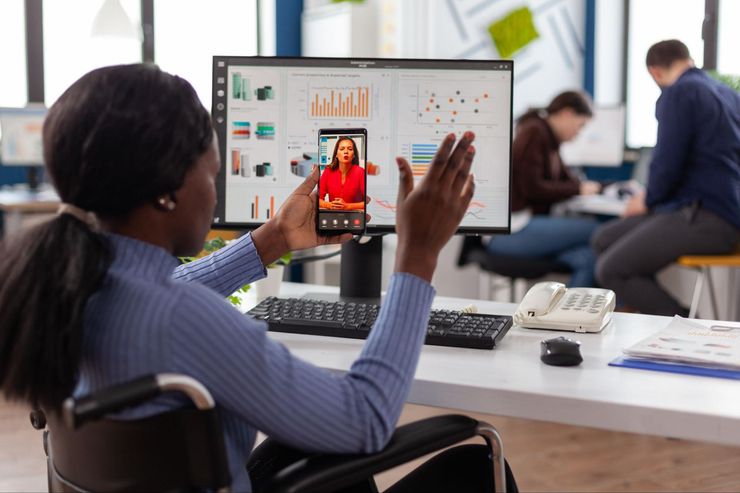 African-American woman wheelchair user, greeting someone on her phone in an office.