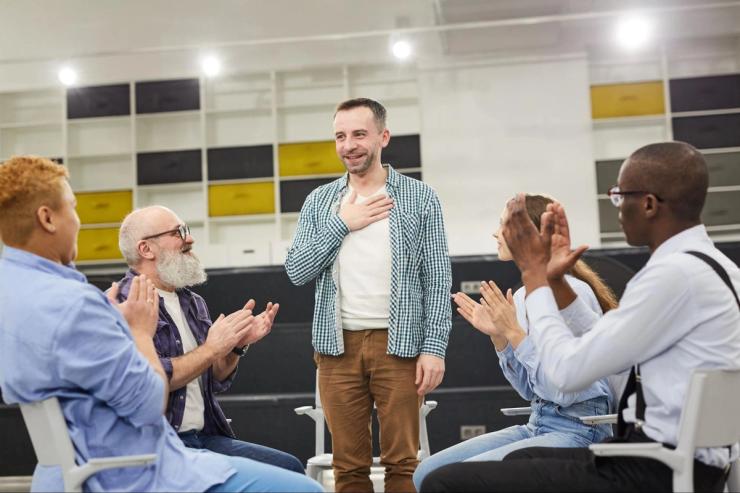 A group of people sitting in a circle with one man standing up. 