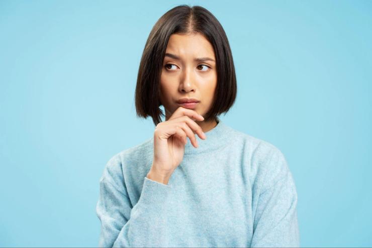 A woman with dark chin-length hair in a blue sweater is staring off into space.