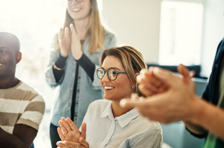 Diverse employees smiling and clapping during an office meeting.