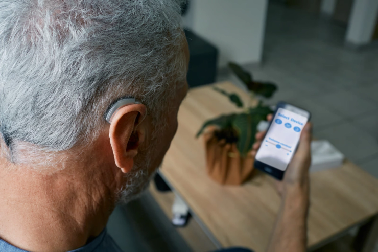 Older adult wearing a hearing aid while viewing live call captions on a smartphone