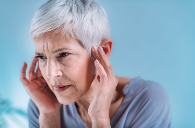 Older woman with short silver hair suffering from tinnitus. She is holding her fingers to temples with a pained look on her face.
