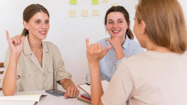 smiley women conversing table using sign language