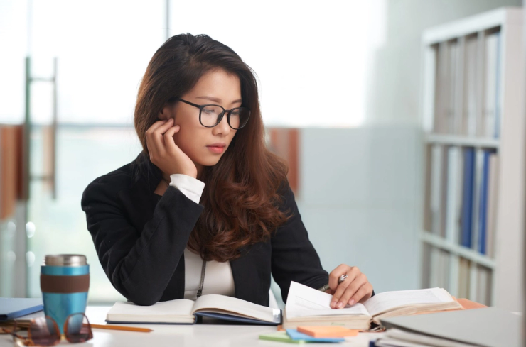 Young female wearing eyeglasses and business attire. She is reading and taking notes. Photo by DragonImages.