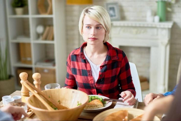 Person sitting quietly at a family dinner table while others talk nearby, illustrating the isolation and communication challenges associated with dinner table syndrome.