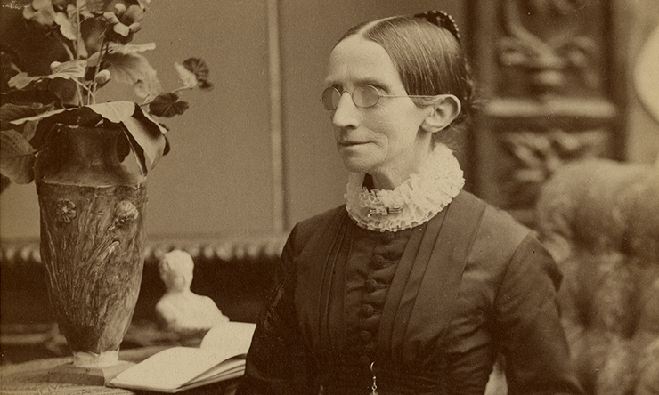 vintage portrait of a woman with glasses in Victorian dress standing beside a vase and open book