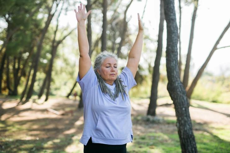 A mature woman outdoors stretching her arms with eyes closed 