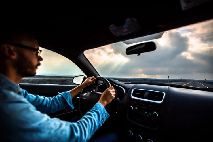 An adult man in a blue shirt is driving a car.