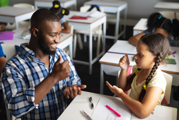 Male teacher using sign language with an elementary girl in the classroom