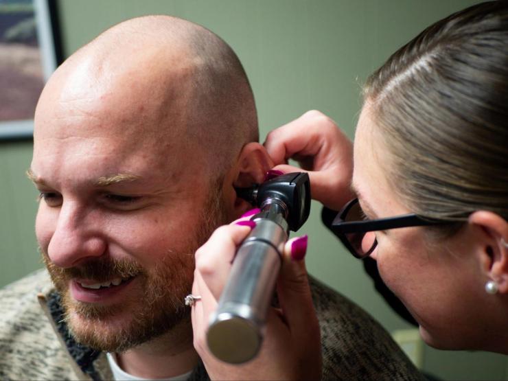 Audiologist examines a man's ear using a handheld instrument.