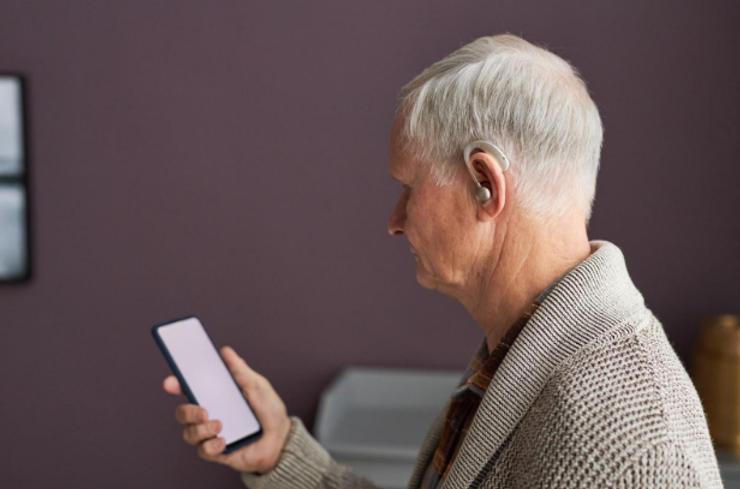 Senior man wearing a hearing aid device and holding an iPhone