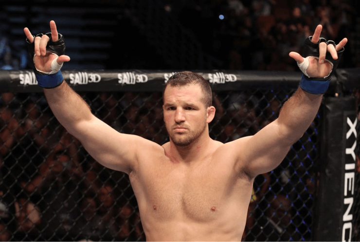 MMA fighter raising both arms in victory inside a UFC octagon after a match