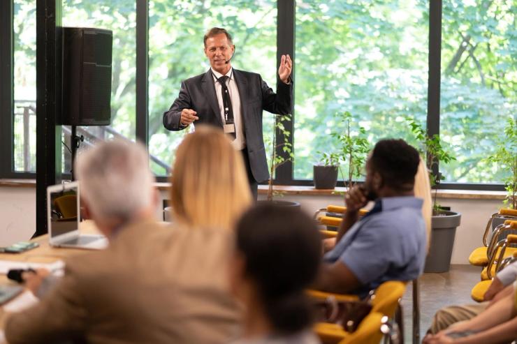 A man in a suit is giving a presentation to a classroom with a microphone. 
