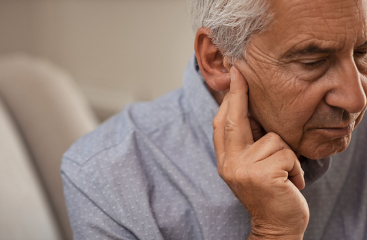 Older man holding his fingertips close to his right ear. 