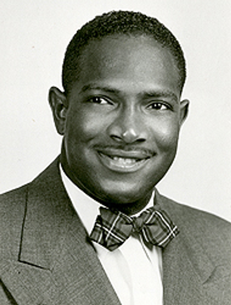 Black and white portrait of a man wearing a suit and bow tie, smiling and facing the camera in a studio setting