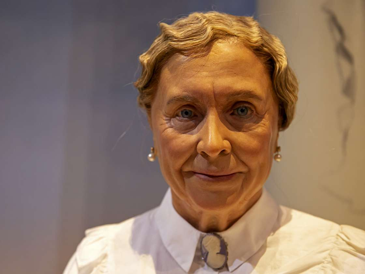 close up of older woman with short wavy hair wearing a high collar blouse and earrings