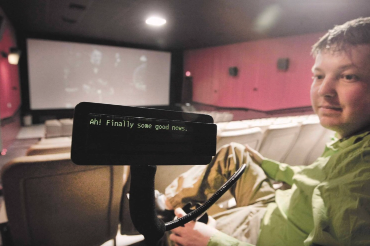 Man using closed captioning device inside a theater.