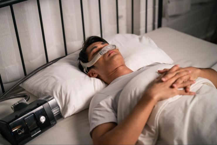 Man sleeping with CPAP machine to improve breathing and sleep quality, supporting overall health and reducing risk factors linked to hearing loss