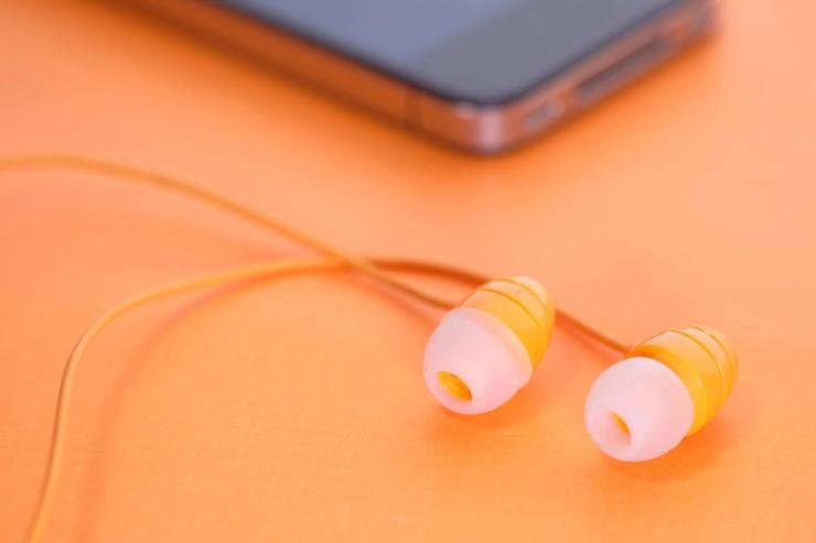 A pair of earbuds next to a smartphone on an orange background.