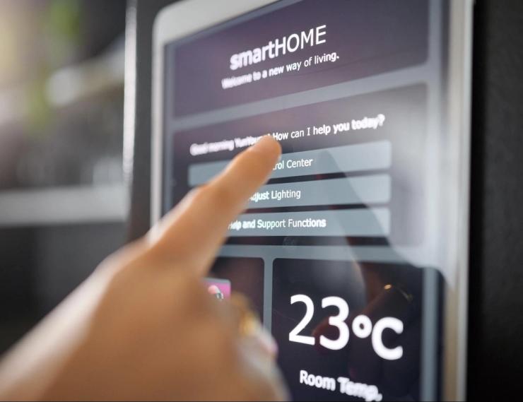 A finger is pushing a button on a smart technology hub device. The room temperature is displayed.