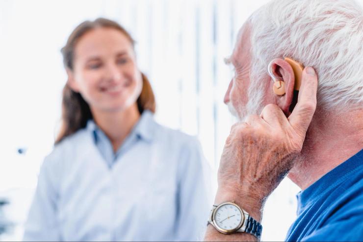 An older man wearing a hearing aid and sitting near a woman.