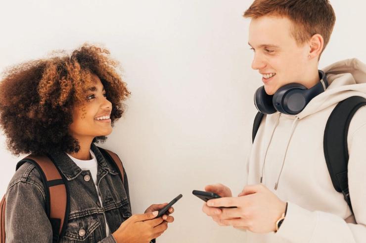 A young female and male looking at each other, holding smartphones.