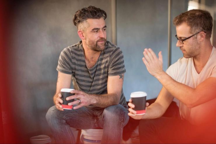Two men are seated having a conversation while drinking coffee. 