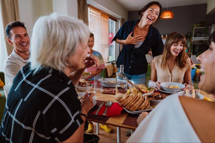 Family gathered around a dinner table talking and laughing, illustrating the fast-paced group conversations that can be difficult for people with hearing loss to follow.