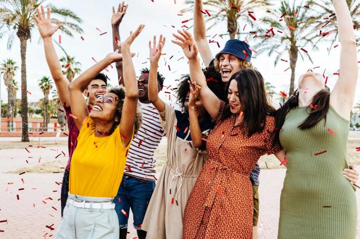 A group of young friends are outside throwing confetti.