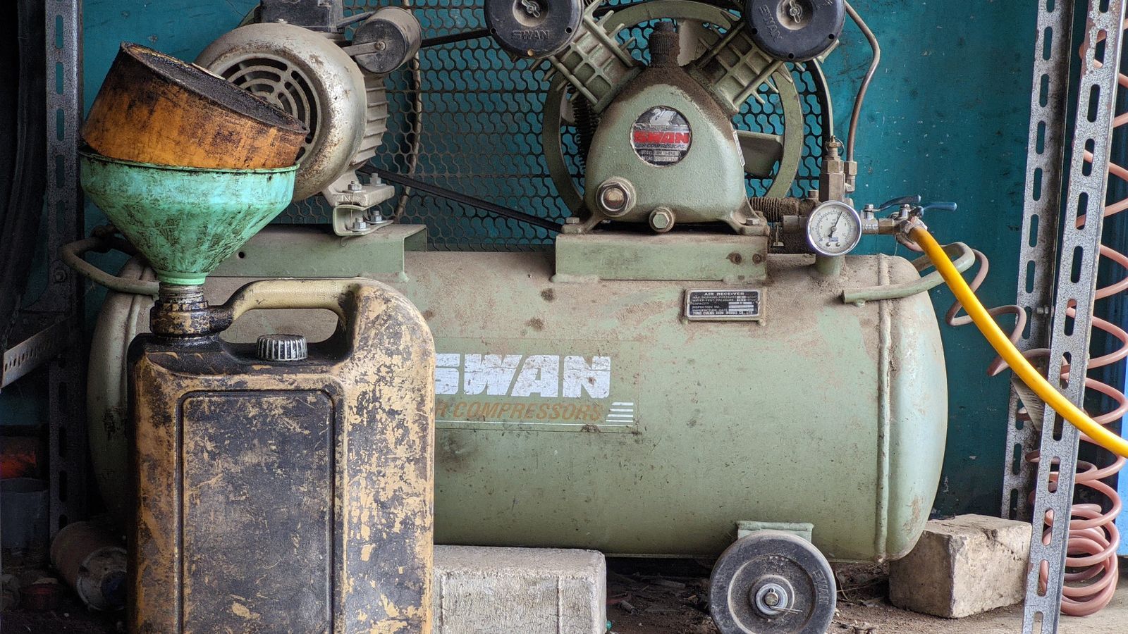 Old industrial air compressor and oil can in a rustic workshop setting. Ideal for industrial themes.