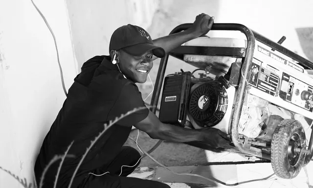 A cheerful young man wearing a cap and earphones operating a portable generator outside.