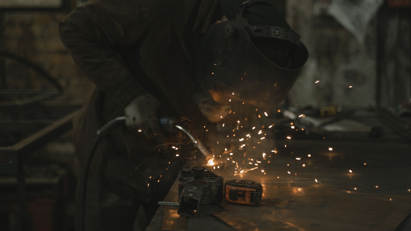 A welder skillfully operates in a dimly lit workshop, surrounded by sparks.