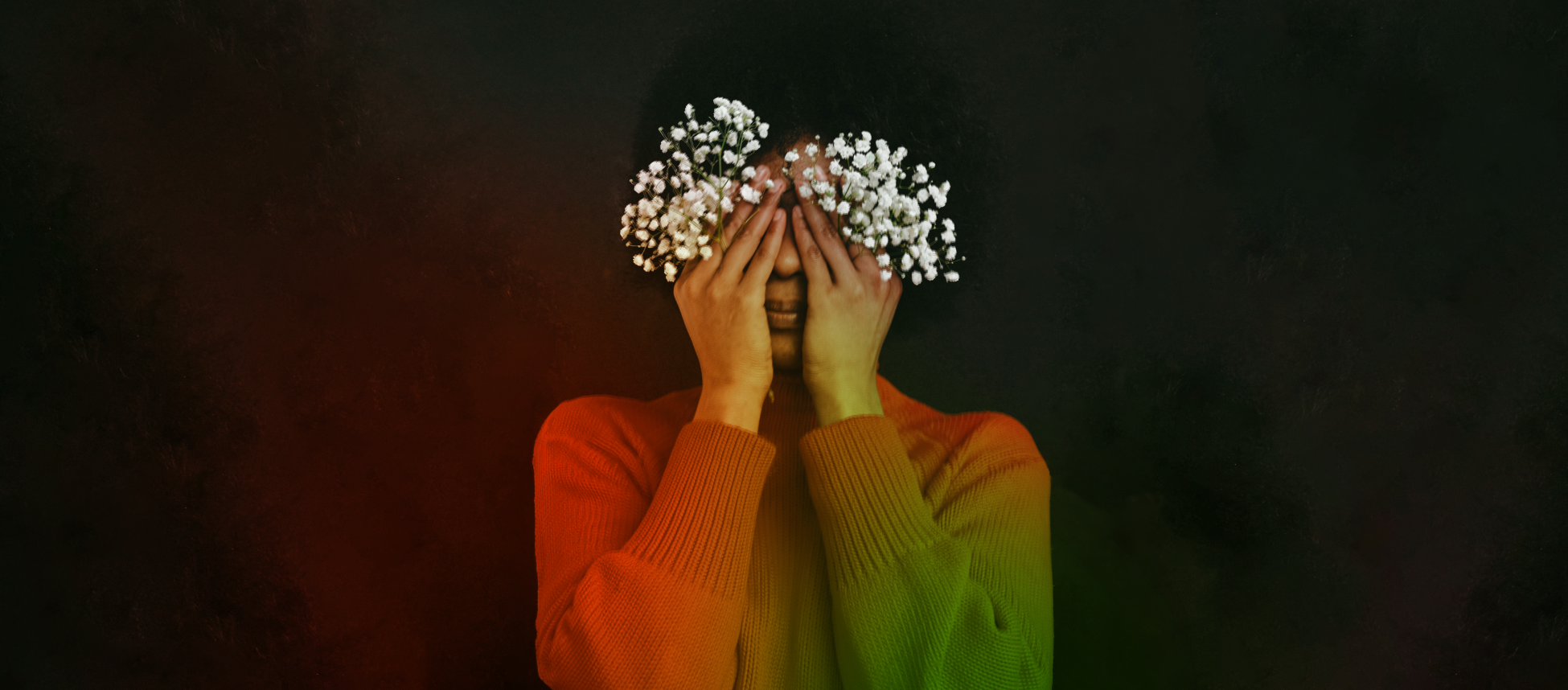 A red and green gradient image of a young person holds baby breath's flowers over their eyes, in front of a black background.