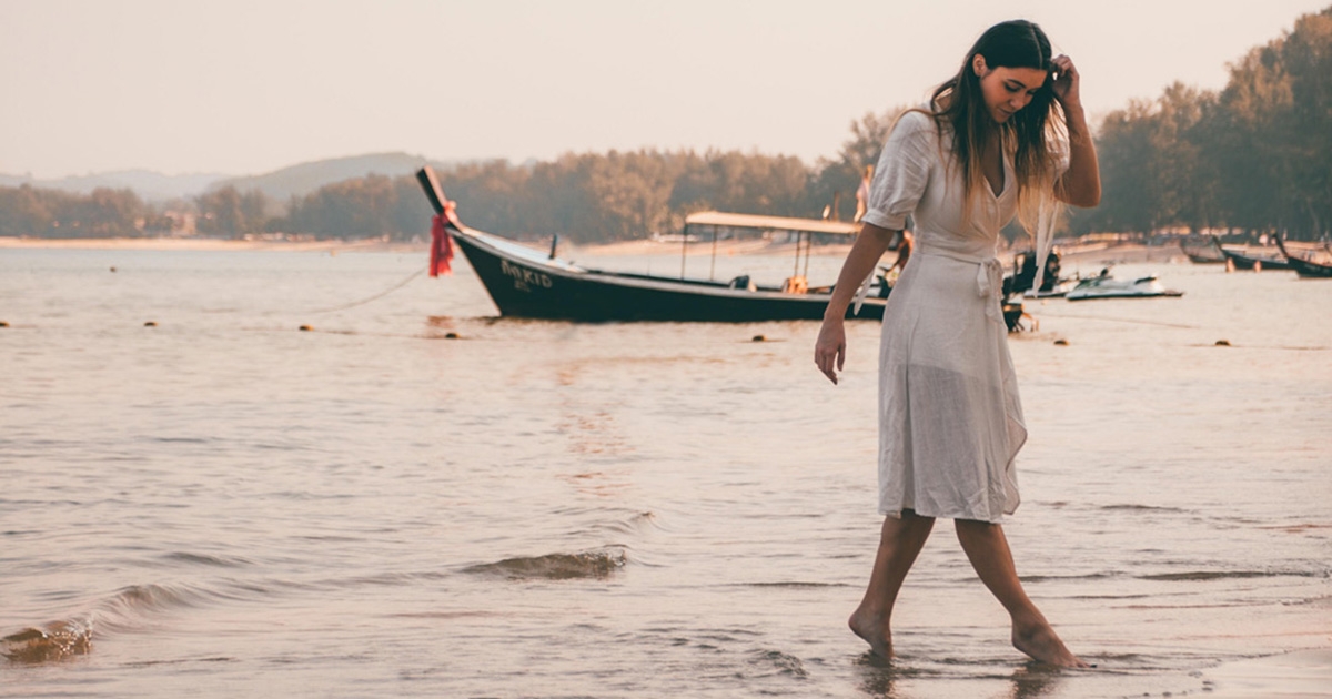 Woman in white dress walking on the shore at a beach