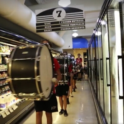 A line of bass drum players marching through a hallway