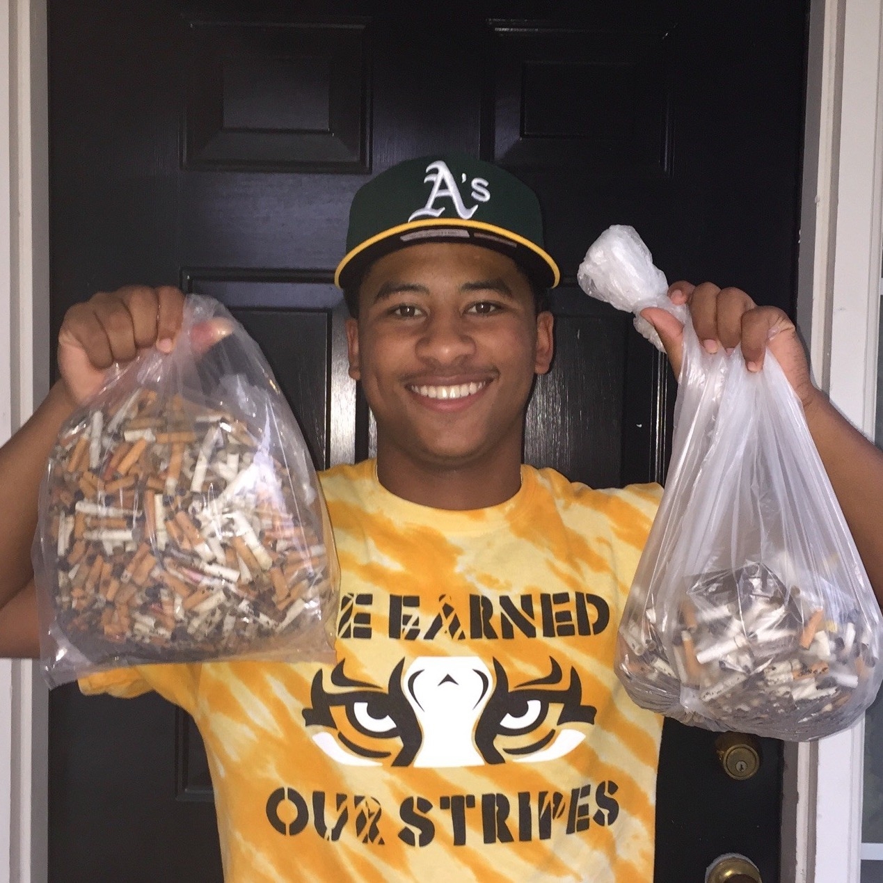 Young person holding up two bags of hundreds of cigarette butts he collected and cleaned up from his community streets