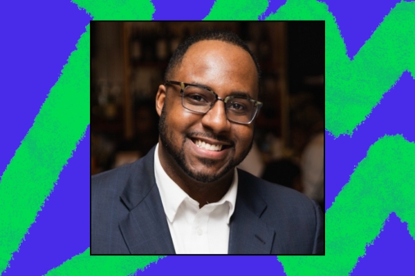A smiling individual wearing glasses and a blazer, representing a welcoming atmosphere for those interested in volunteer and community service opportunities. The colorful background suggests an energetic, engaging environment for civic learning and leadership programming.