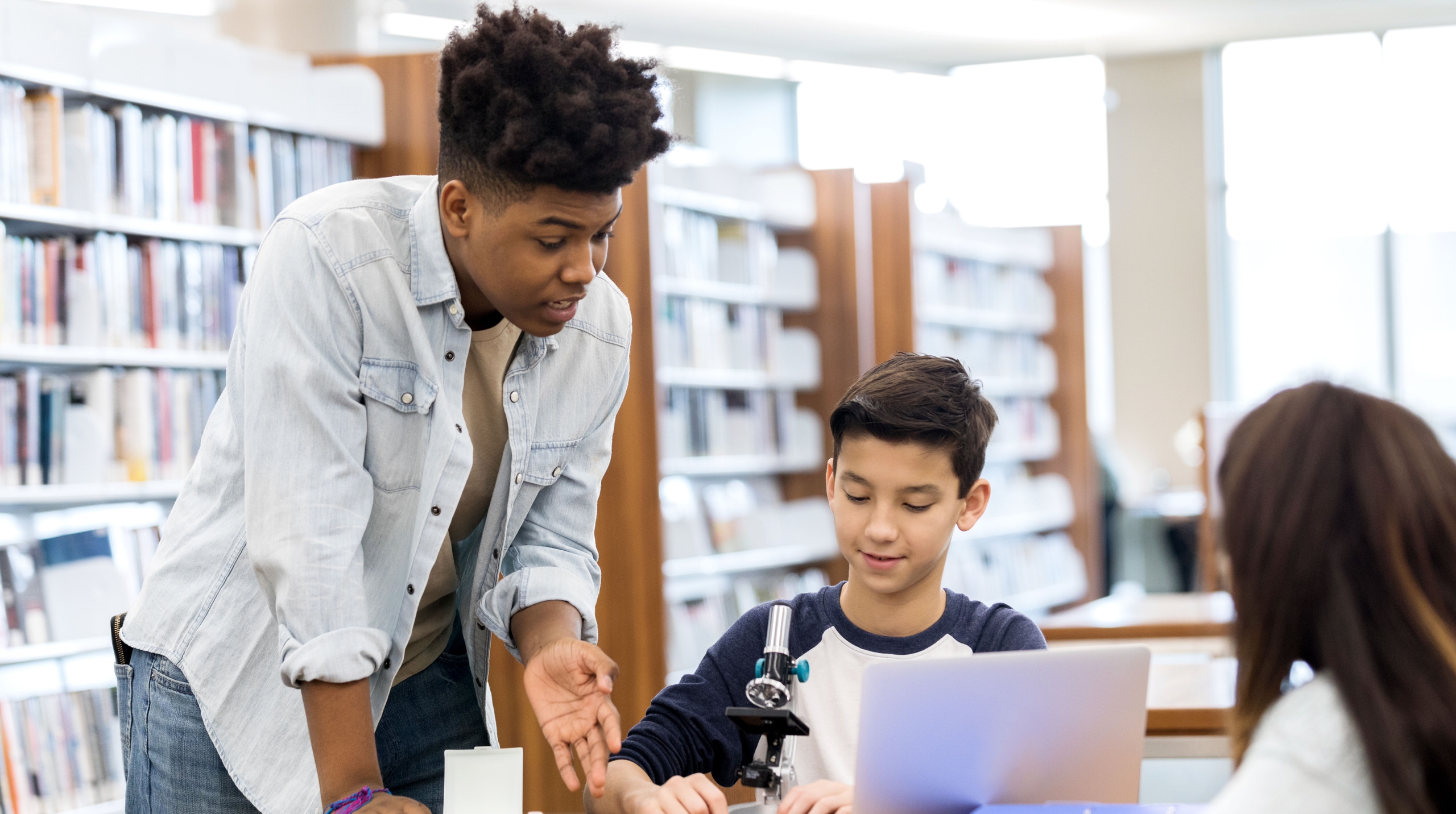 One standing person is guiding a second person at a computer to search for volunteer opportunities while a third person looks on.