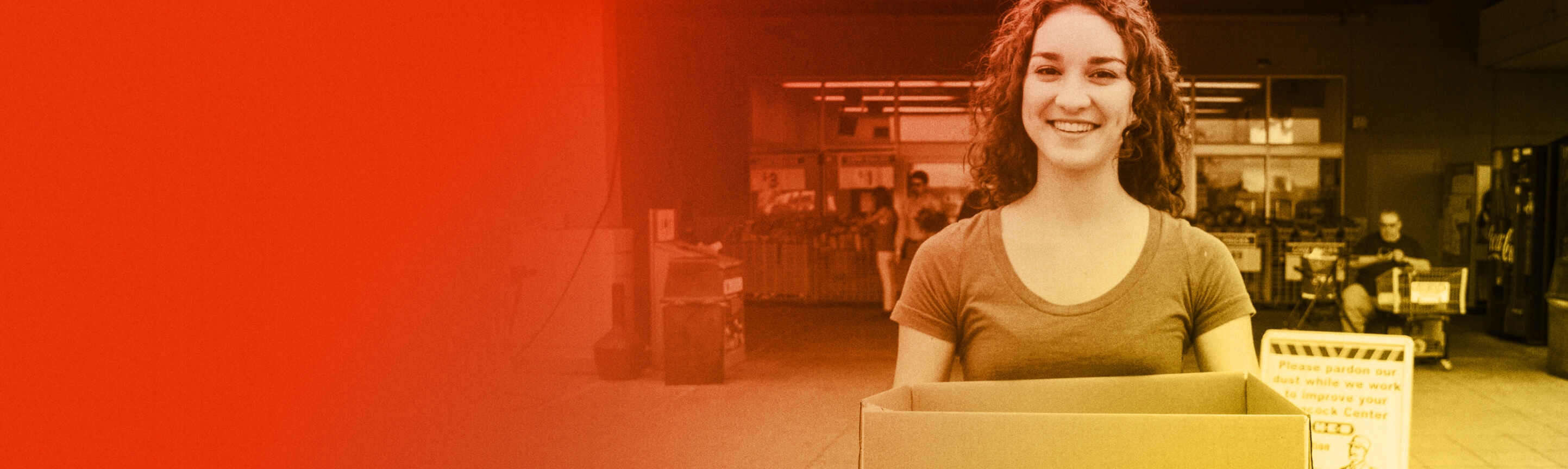 A person standing outside a store holding a cardboard box to collect food from others who are walking by.