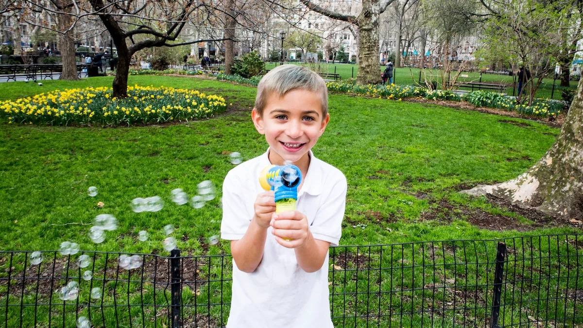 Young boy in a city park with a bubble blaster toy, filling the air with bubbles