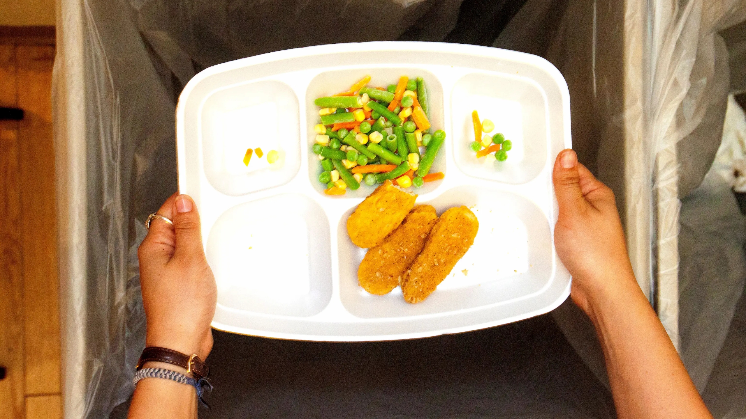 Someone holding a tray of cafeteria food, poised to throw the tray in a trash barrel