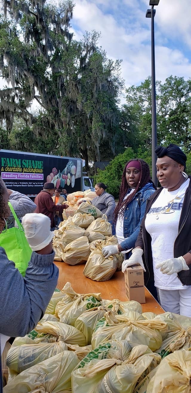 A diverse group of volunteers sorting and distributing food packages at a community service event. Bags filled with food items are prominently displayed on a table, surrounded by participants actively engaging in the process.