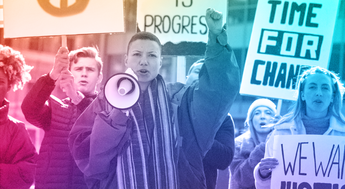 A group of protesting and yelling young people in cold weather clothing, one person has a megaphone while others carry signs. One sign reads "time for change"